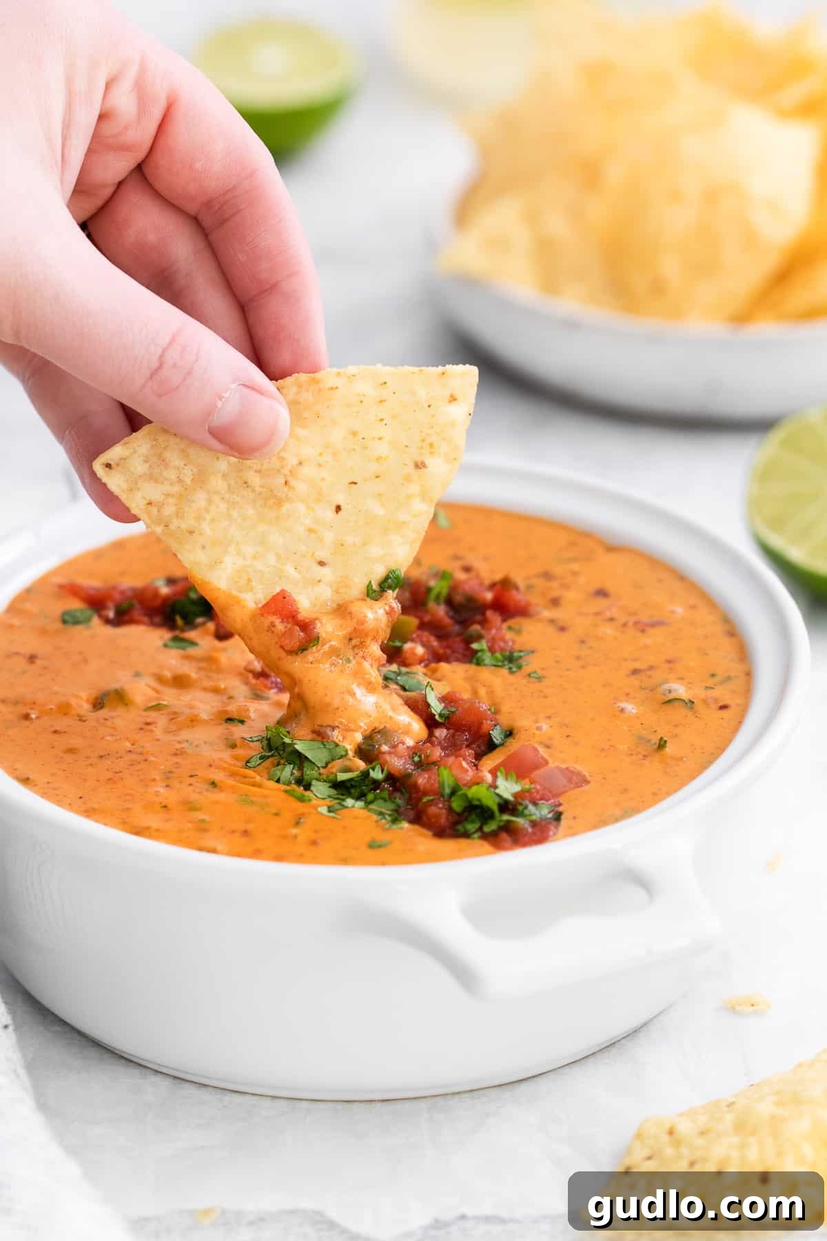 Velveeta Dream Dip 7 A hand scooping a generous portion of Velveeta cheese dip with a crunchy tortilla chip, highlighting the rich texture.