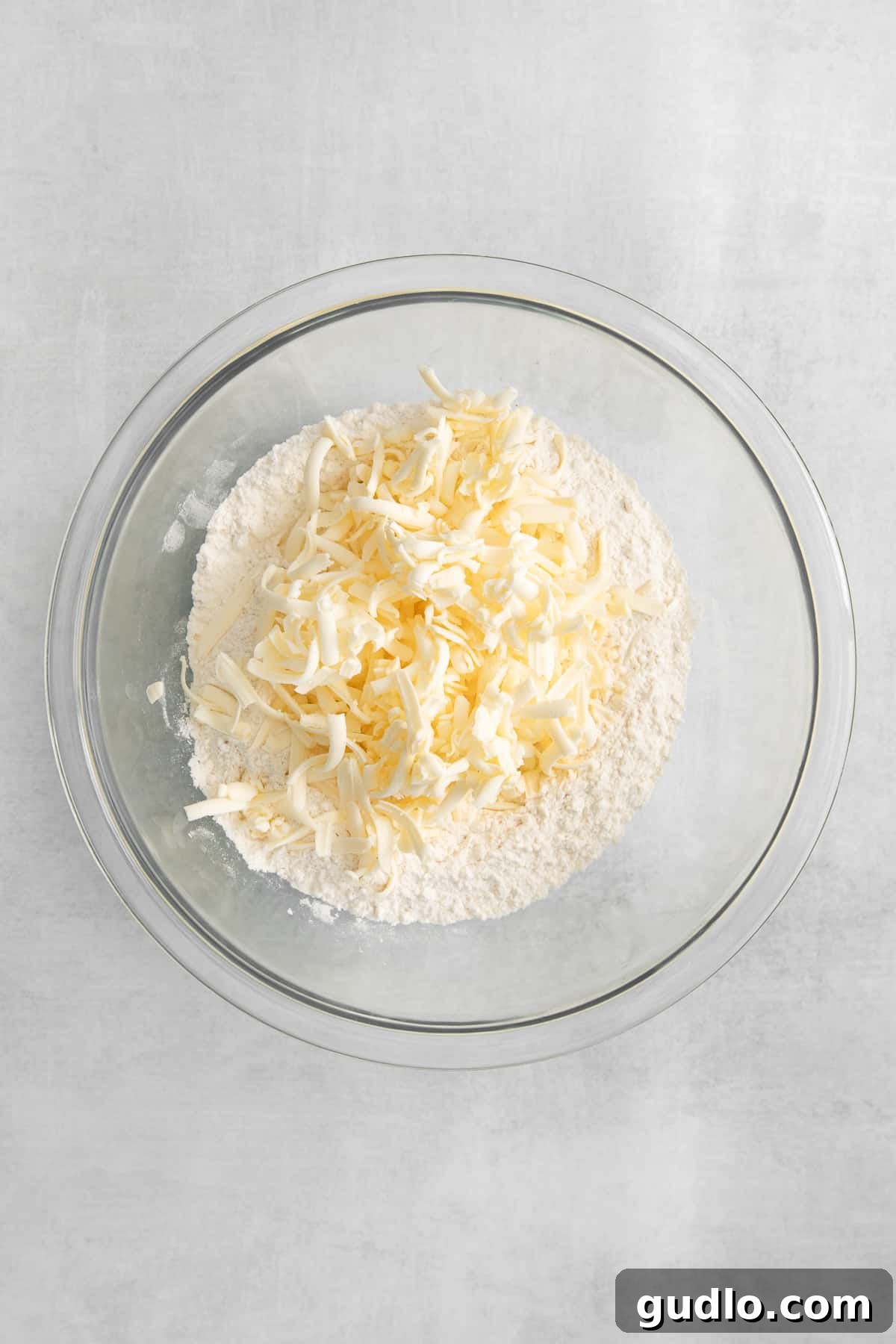 A close-up shot of grated cold butter expertly mixed with all-purpose flour and kosher salt in a spacious mixing bowl, creating a coarse texture before the addition of liquid.
