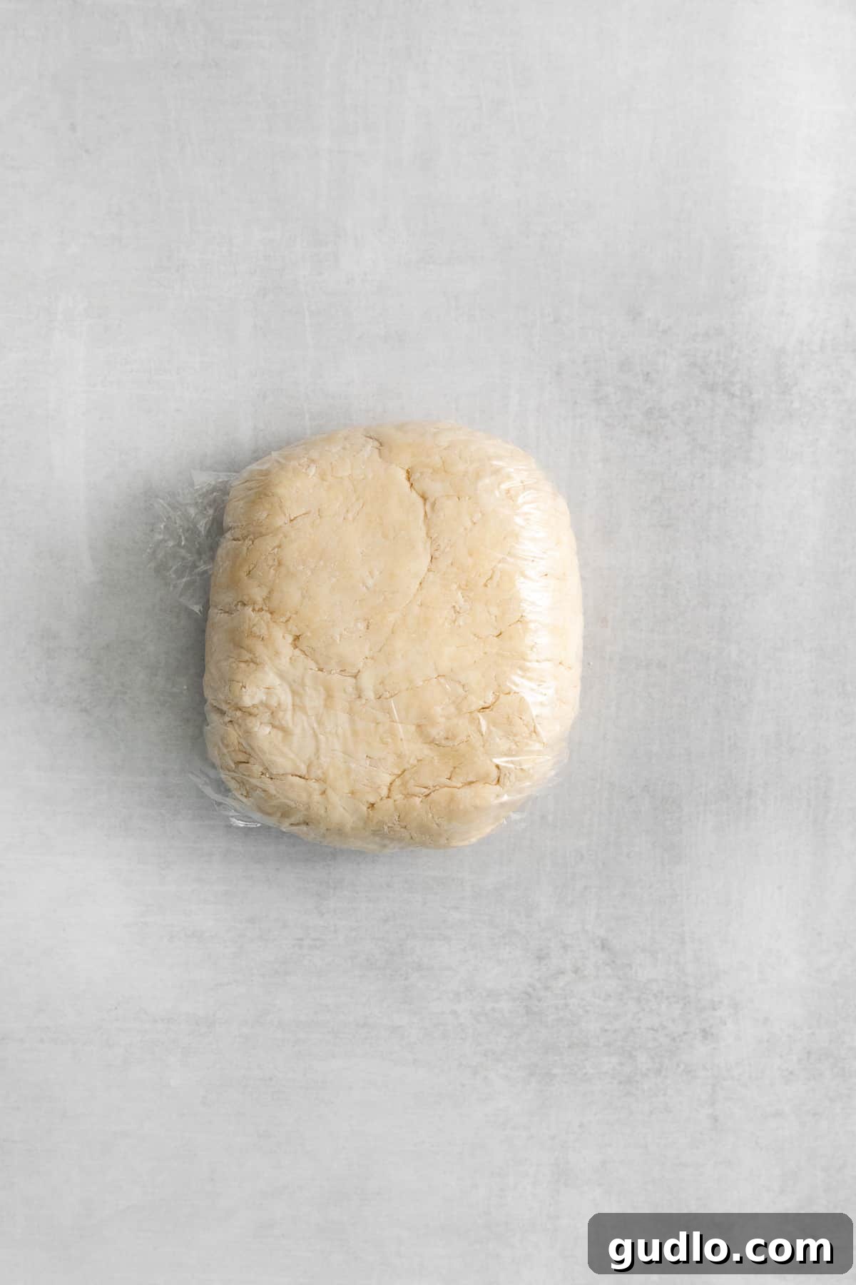 Homemade puff pastry dough, expertly folded into multiple layers and tightly wrapped in plastic wrap, chilling in the refrigerator to ensure the butter firms up and gluten relaxes.