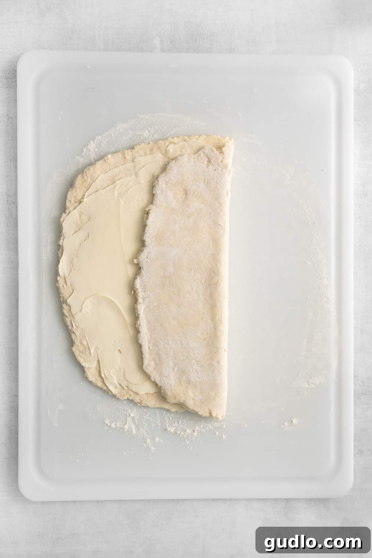 A sheet of puff pastry dough with softened butter meticulously spread over two-thirds of its surface, demonstrating a crucial step in the lamination process before folding.