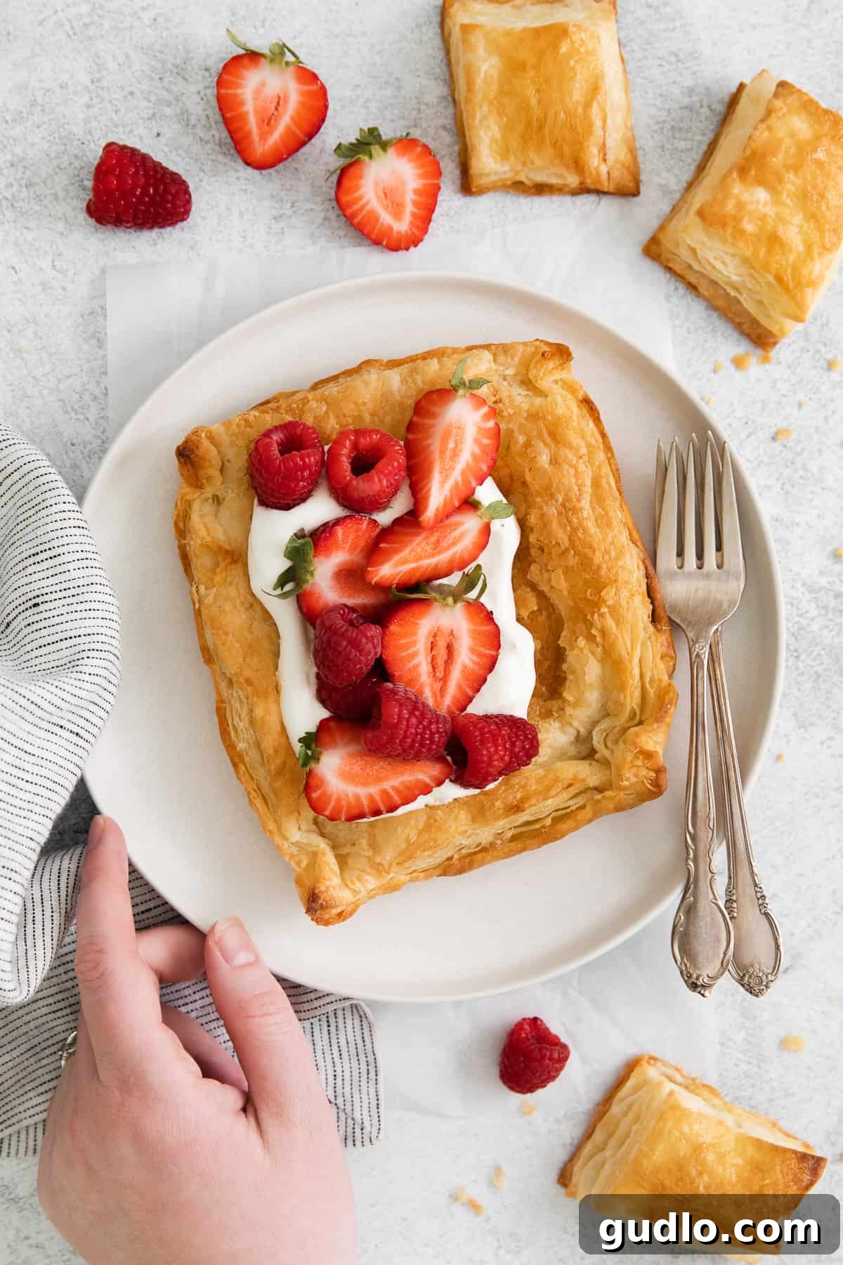 A beautiful serving of baked homemade puff pastry, garnished with fresh whipped cream and an assortment of vibrant berries, elegantly presented on a white plate, ready for a delightful dessert.