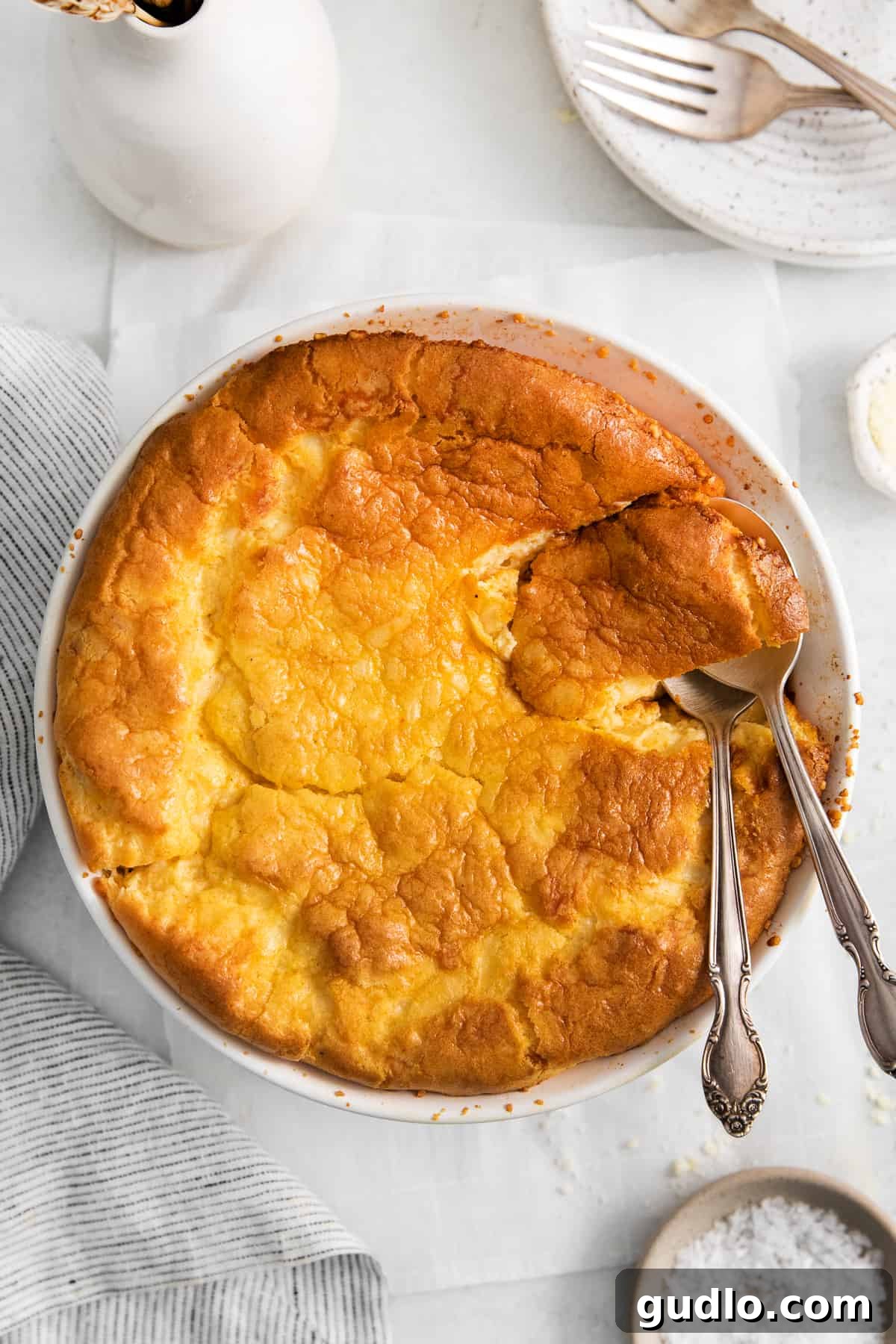 A golden-brown cheese soufflé, perfectly puffed and airy, presented in a round white casserole dish.