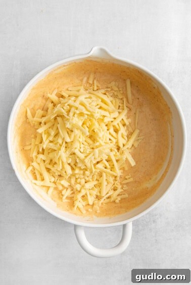 Shredded cheeses and seasonings mixed into a creamy base in a white bowl.