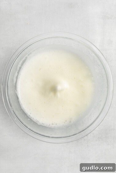 Whipped egg whites in a glass bowl, showing soft peaks.