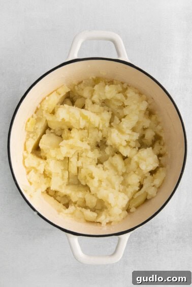 Mashing potatoes in a pot with a potato masher.