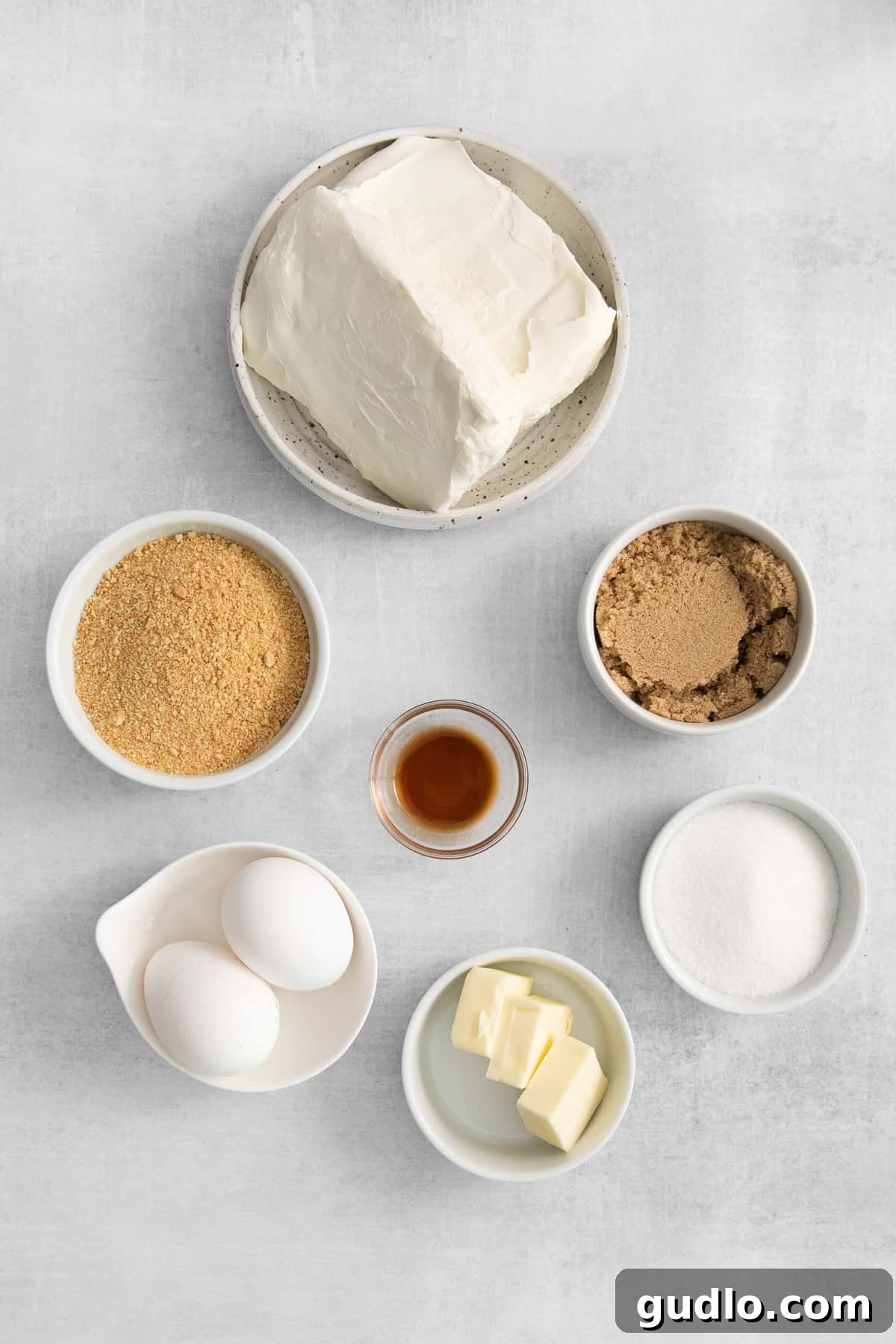 A selection of essential ingredients for mini cheesecakes laid out in small bowls.