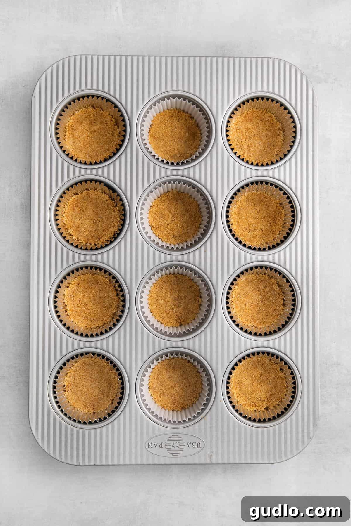 Graham cracker crusts pressed into a mini muffin tin, ready for filling.
