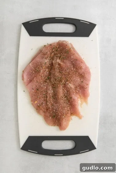 A cutting board with a piece of seasoned turkey breast on it.