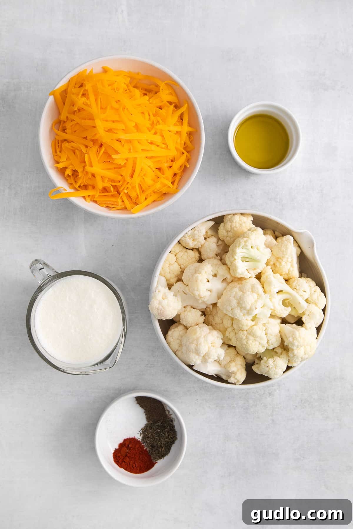 Various ingredients for cauliflower mac and cheese laid out in bowls, including chopped cauliflower, shredded cheese, and spices.