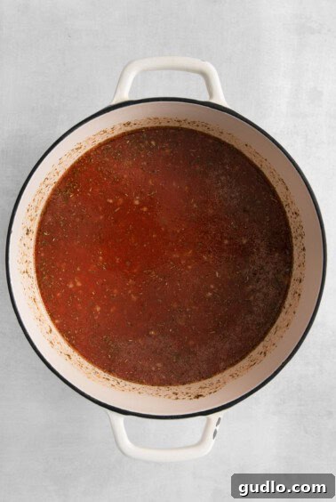 Soul-Satisfying Tortellini Soup 5 a pot of tomato sauce on a white surface.