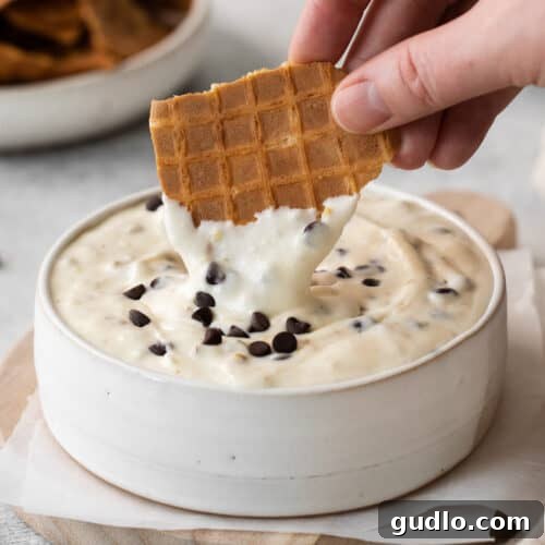 A waffle cone being dipped into the creamy cannoli dip, showcasing the delightful texture.