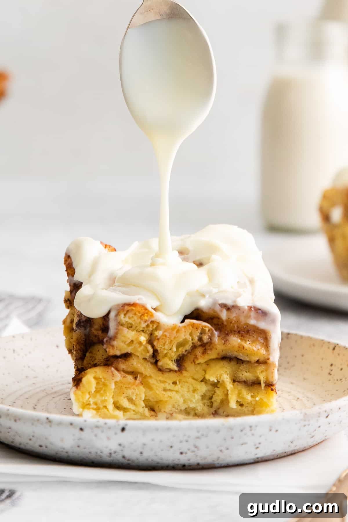 The ultimate cinnamon roll casserole, baked to perfection and topped with sweet cream cheese frosting. A slice of cinnamon roll casserole topped generously with icing, served on a plate.