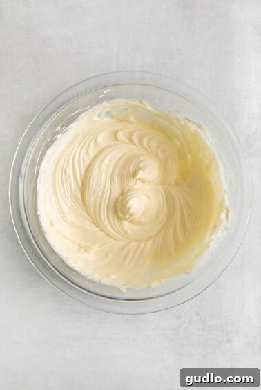 Decadent Cinnamon Roll Bake 5 Whipped cream cheese frosting in a glass bowl, ready to be applied.