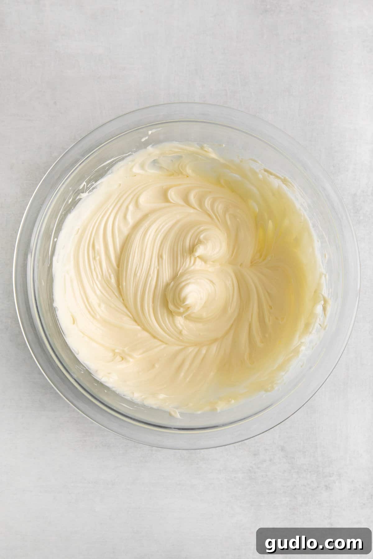 Decadent cream cheese icing for a perfect cinnamon roll casserole. Creamy white icing for cinnamon roll casserole in a glass bowl, ready to be spread.