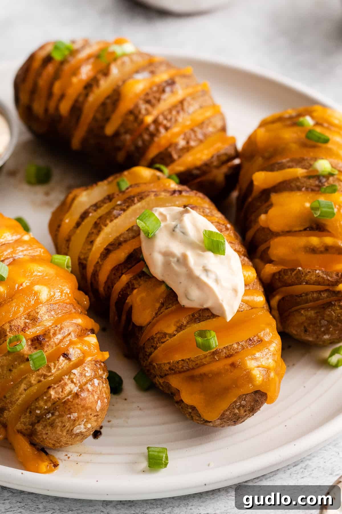 Cheesy hasselback potatoes on a plate, garnished with green onions.