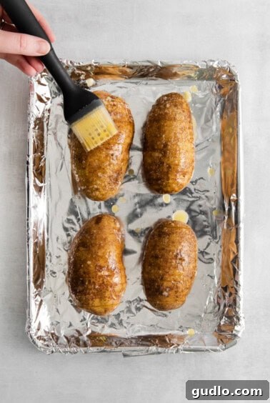 a person using a spatula to brush the potatoes on a baking sheet.