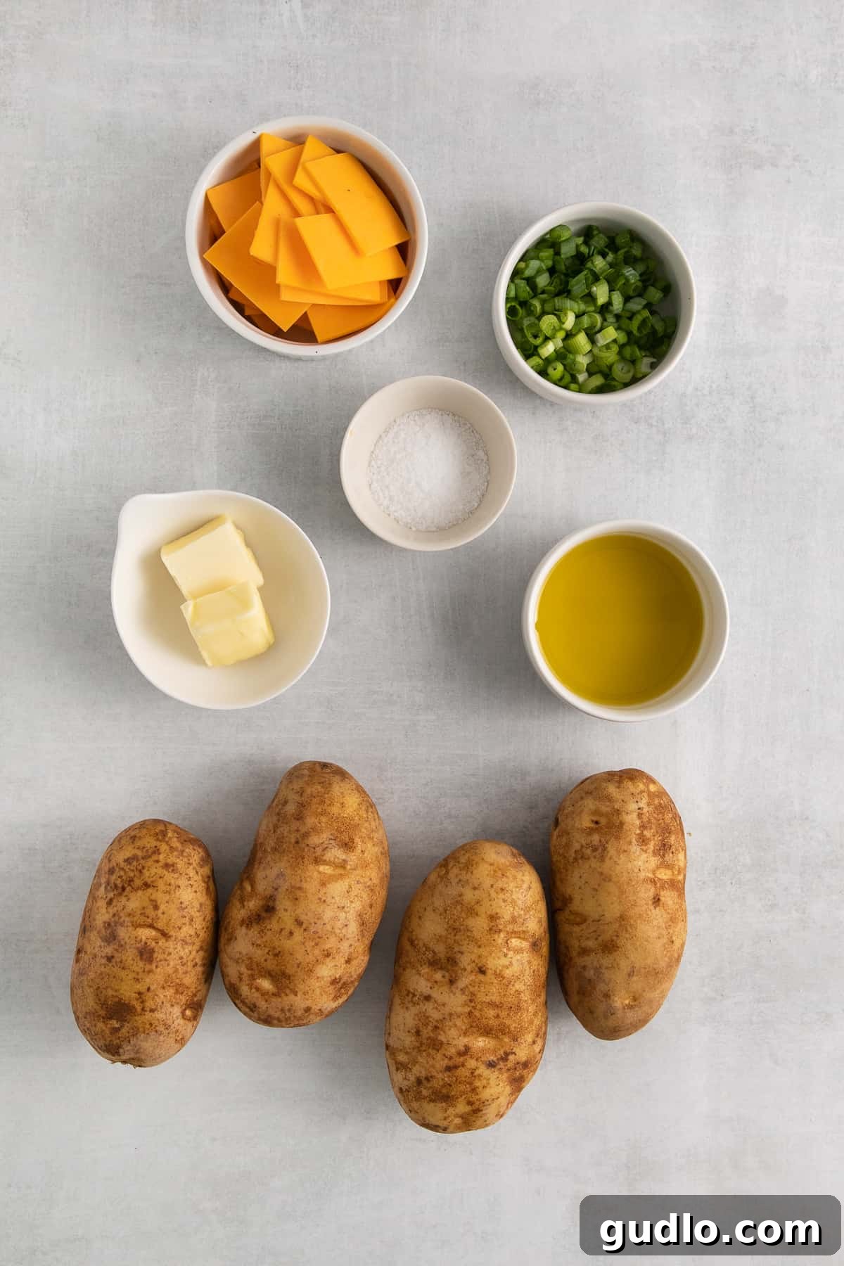 Ingredients for cheesy hasselback potatoes laid out on a wooden surface.