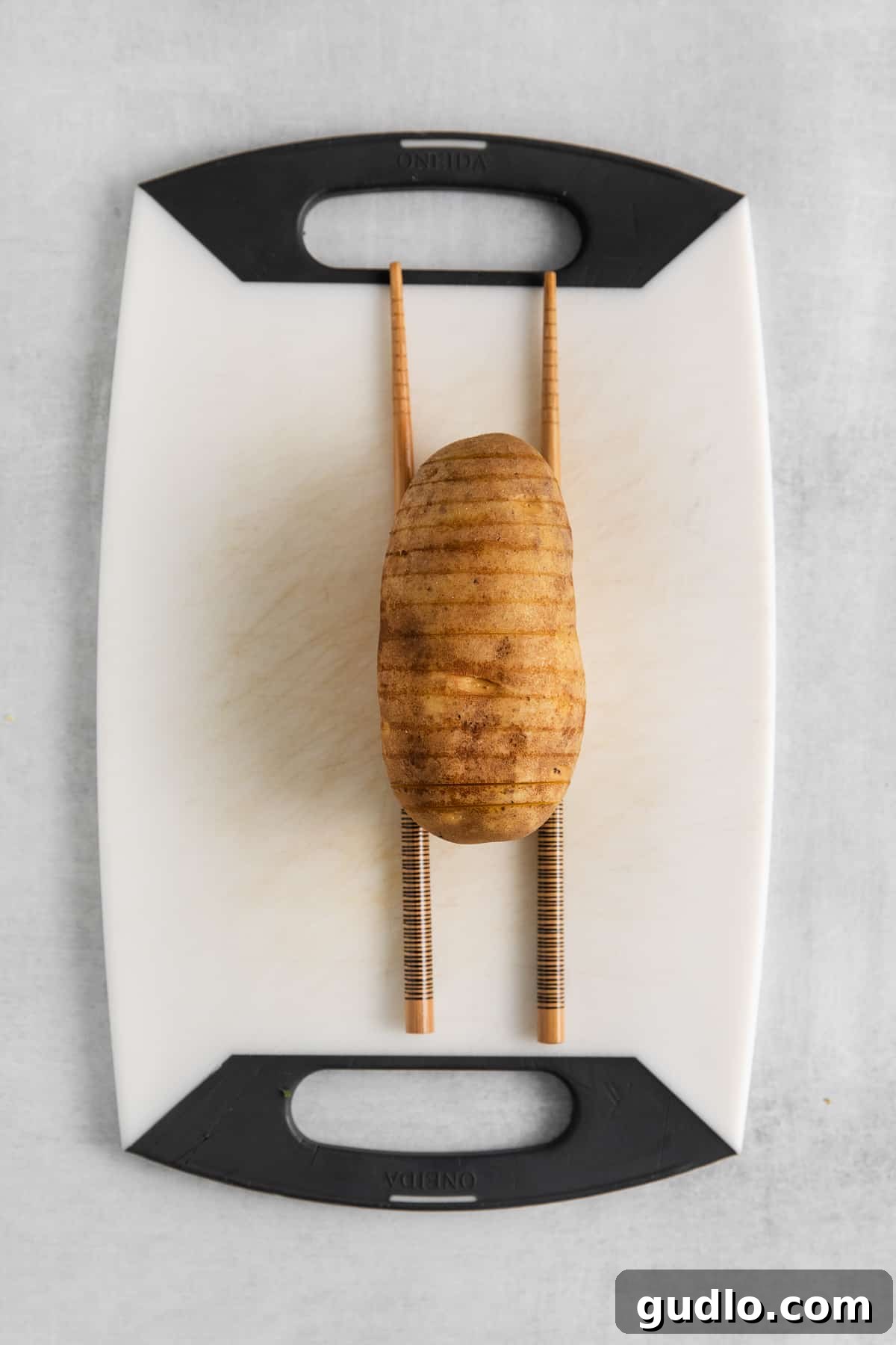 A Russet potato perfectly sliced hasselback style on a cutting board, ready for baking.