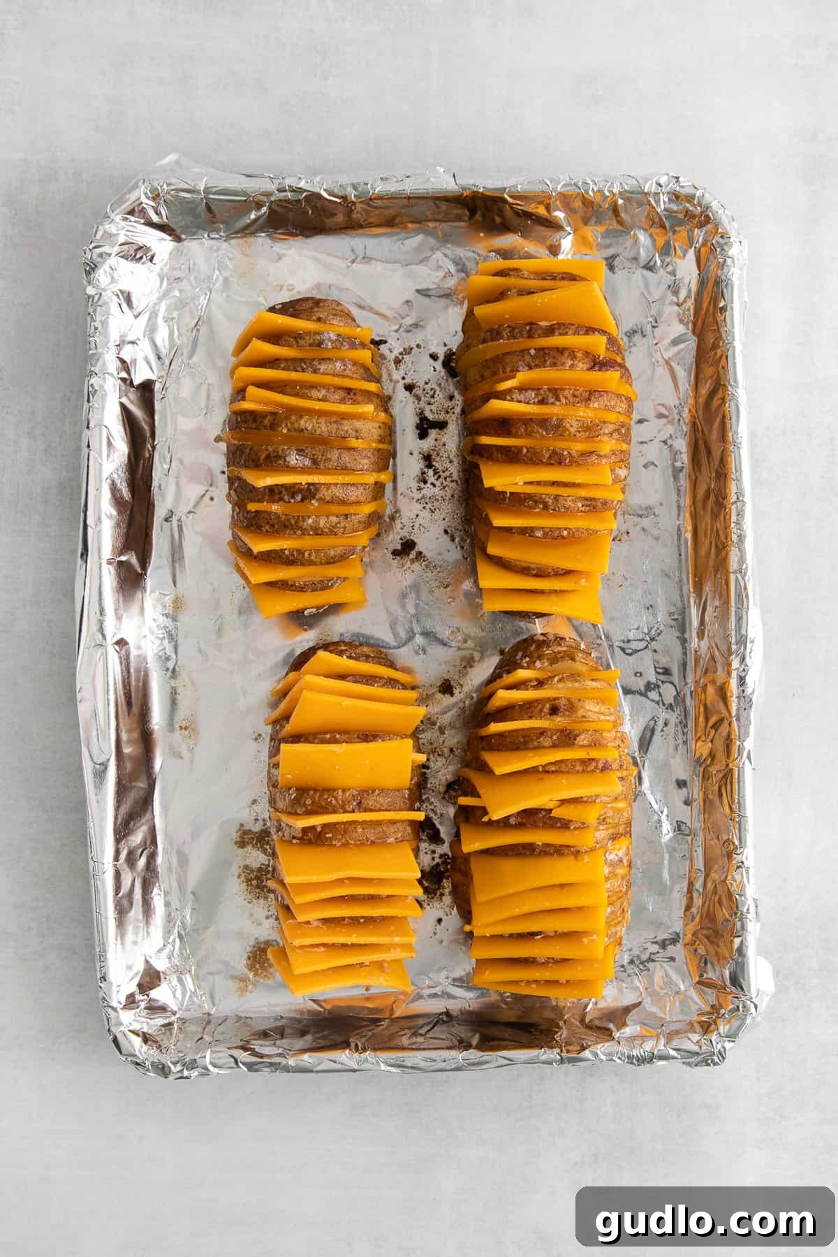 Hasselback potatoes with melted cheese on a baking sheet, fresh out of the oven.