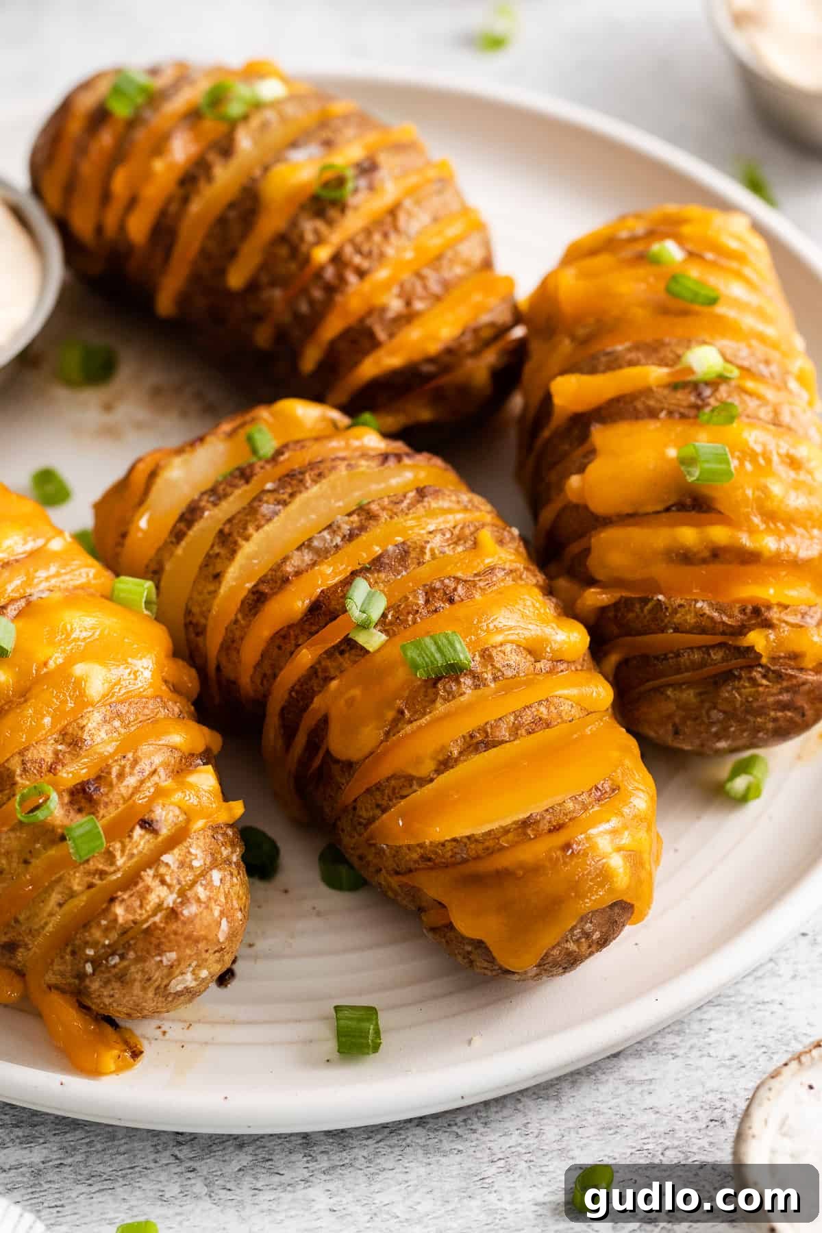 A plated hasselback potato topped with sour cream and chives, ready to eat.