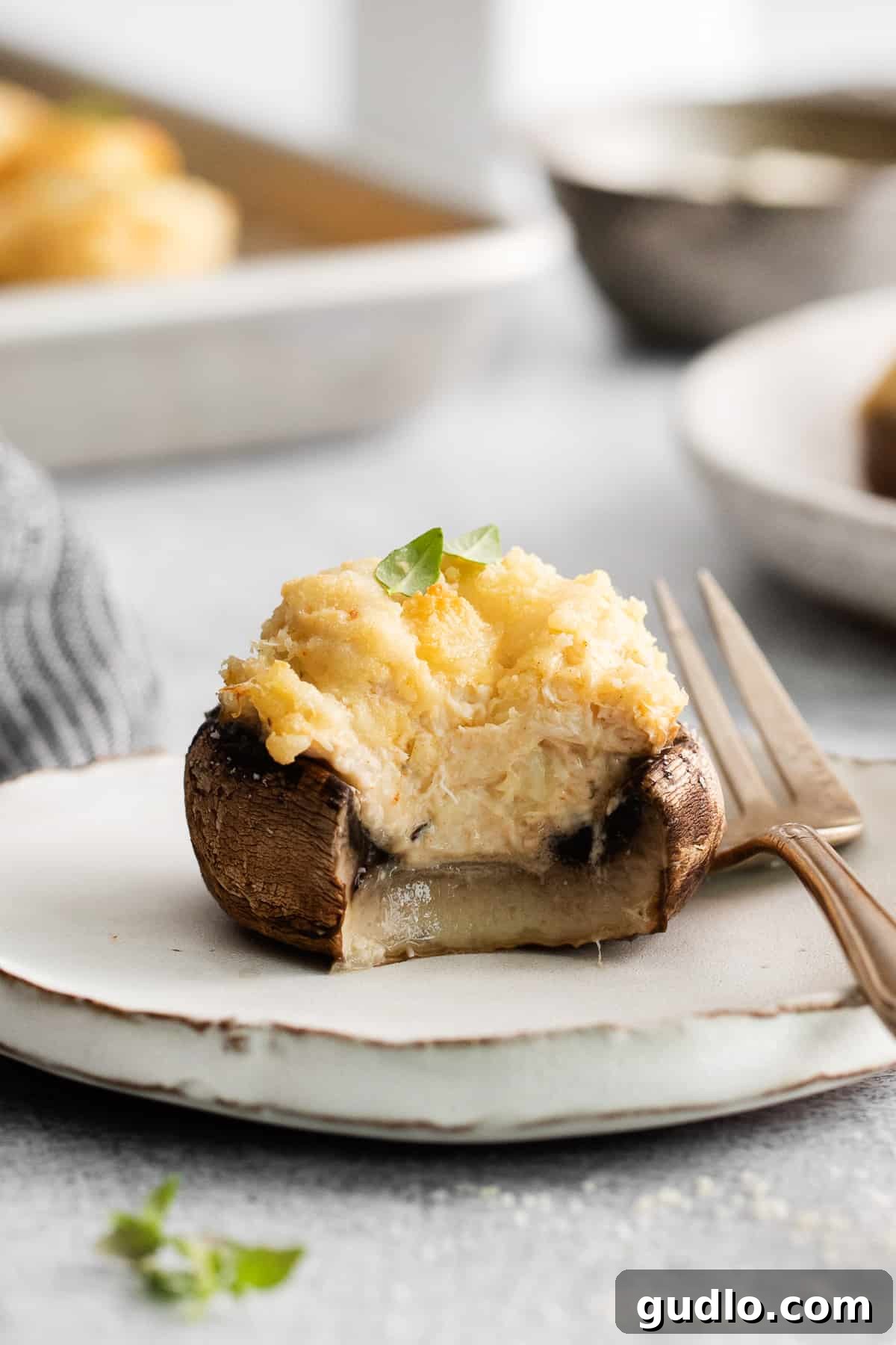 A baked crab stuffed mushroom with a bite taken out, showing the rich creamy filling inside.