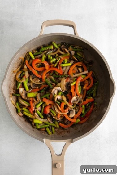 A frying pan filled with colorful, sautéed vegetables and mushrooms, ready for the crepe filling.