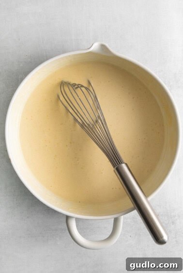A white bowl with crepe batter and a whisk in it, showcasing the smooth consistency.