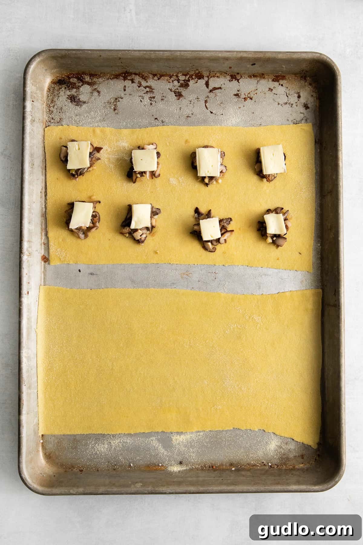 Uncooked mushroom ravioli laid out on a baking sheet, dusted with semolina flour.