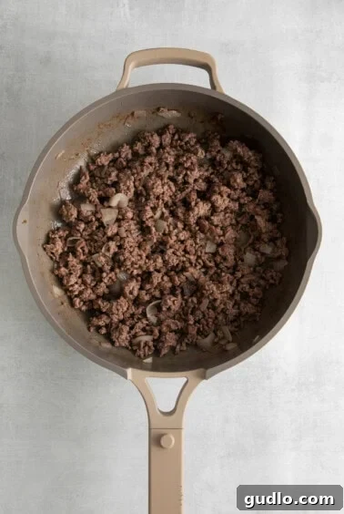 A frying pan with browned ground beef and onions.