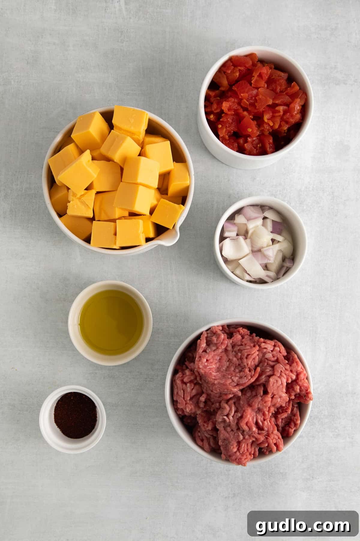 Individual bowls showcasing the essential ingredients for Rotel dip: cubed Velveeta, cooked ground beef, diced yellow onion, and a can of Rotel tomatoes.