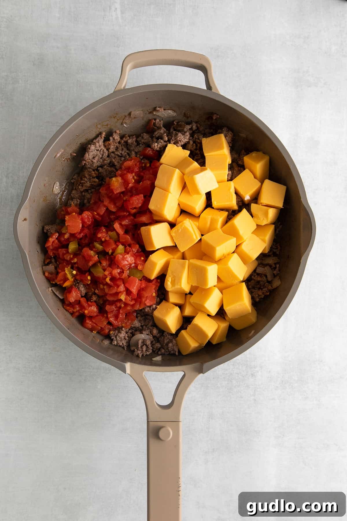 Sautéed ground beef and diced onions mingling with cubed Velveeta cheese as it begins to melt in a large skillet.