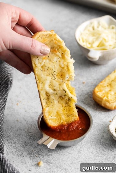 A hand dipping a golden brown Italian dunker into a small white bowl of red marinara sauce.