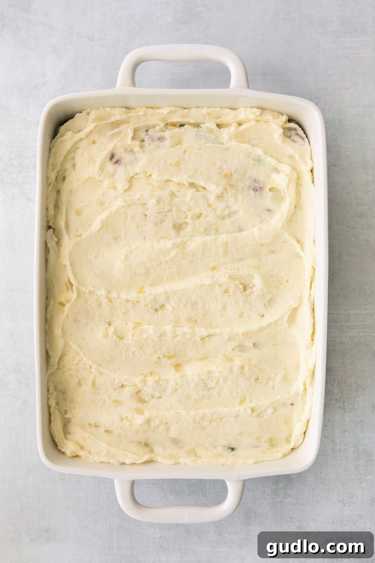 Golden-Topped Cheesy Shepherd's Pie 5 Fluffy mashed potatoes spread evenly over the meat and vegetable filling in a casserole dish, ready for baking.