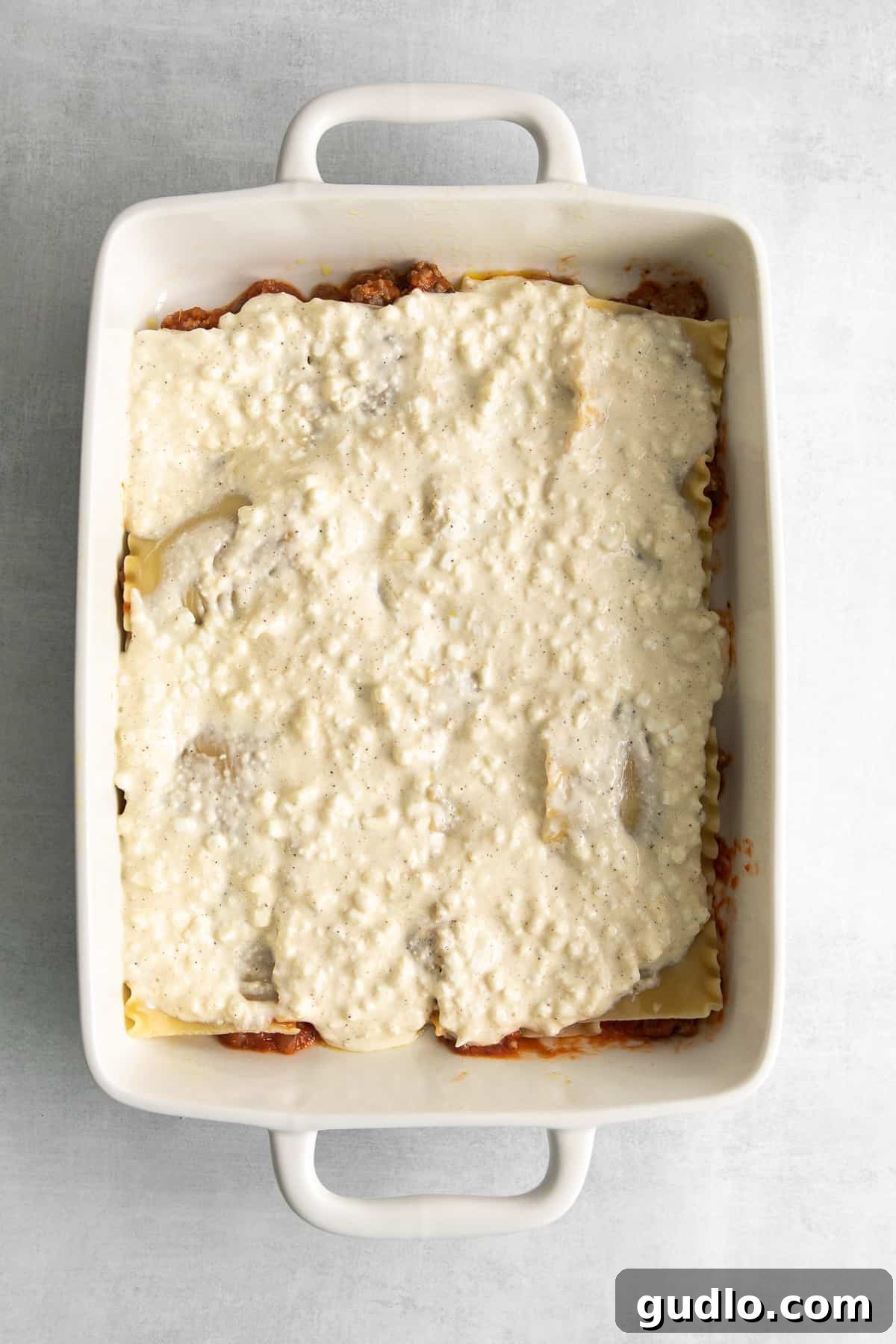 Homestyle Cottage Lasagna 5 A casserole dish being layered with lasagna noodles, savory meat sauce, and the creamy cottage cheese mixture.