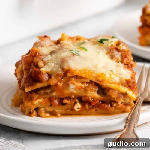 Homestyle Cottage Lasagna 9 A delectable close-up of a slice of cottage cheese lasagna on a white plate with a fork, ready to be eaten.