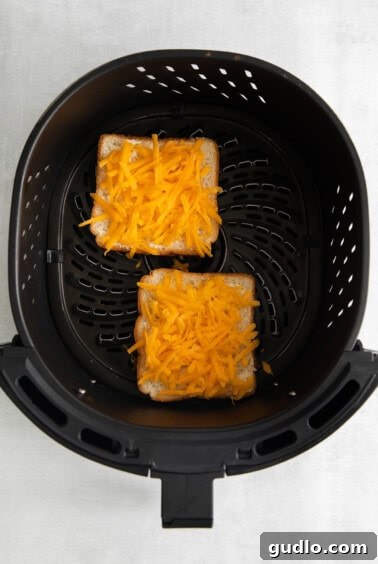 Two slices of bread and cheese in an air fryer, midway through cooking.