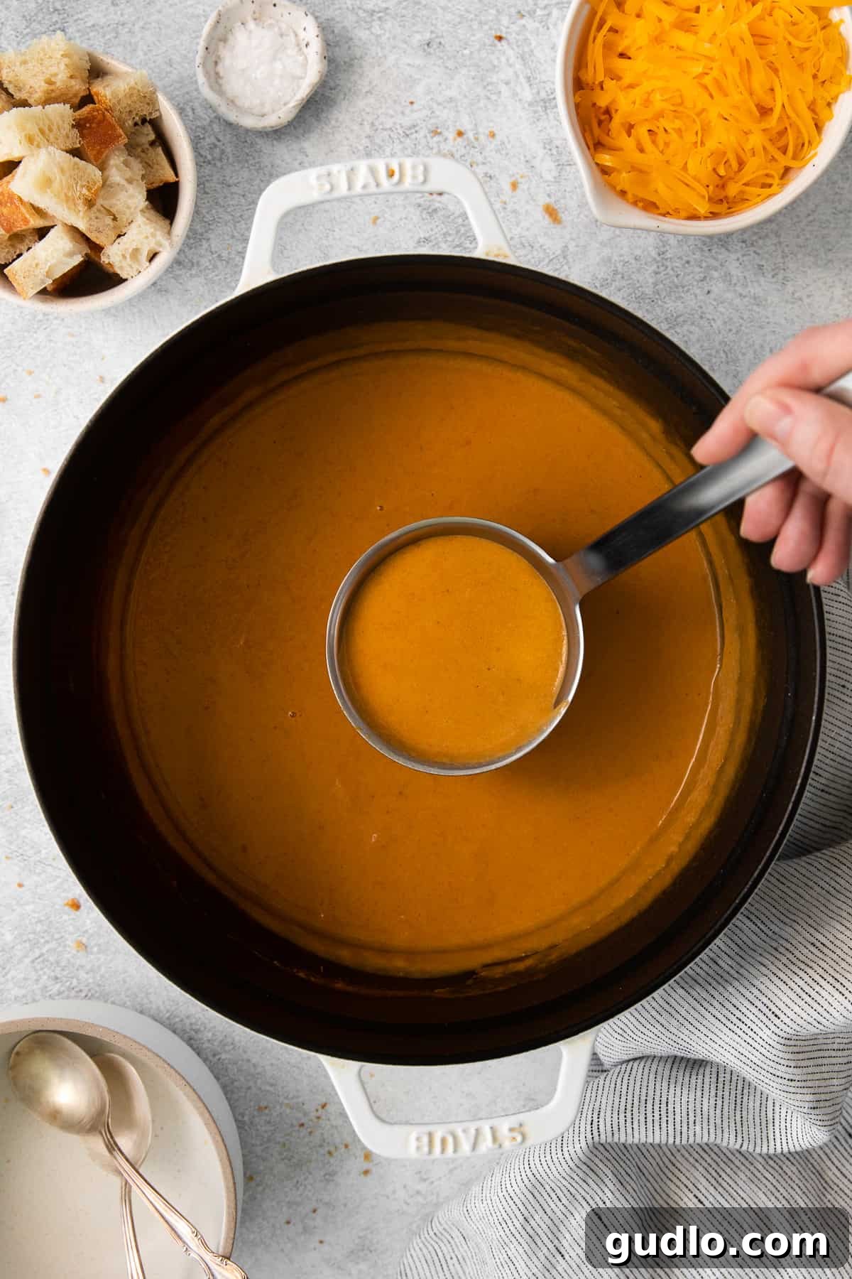 A ladle scooping creamy Wisconsin cheese soup, showing its rich, thick consistency.