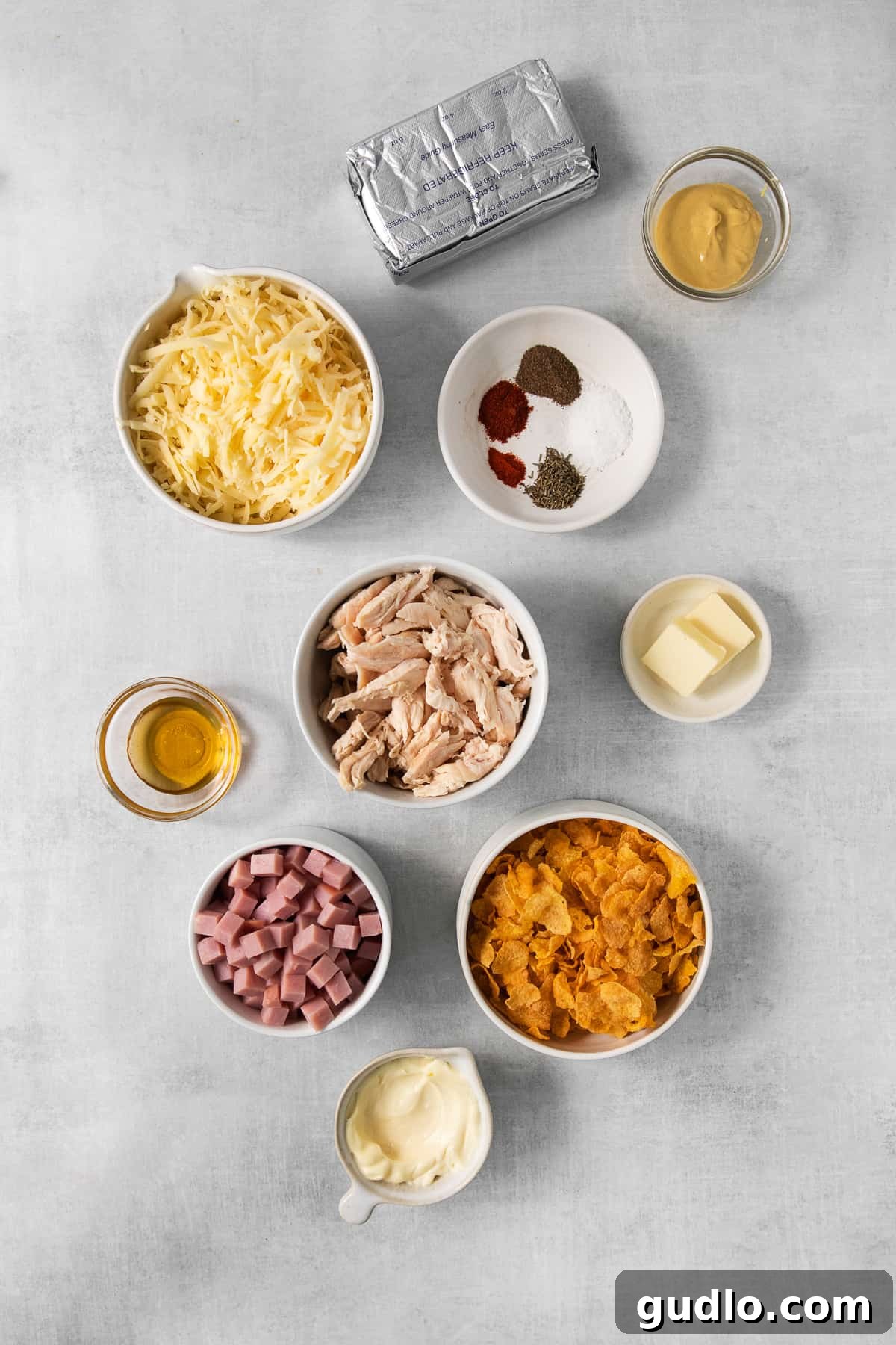 Various ingredients for chicken cordon bleu casserole, including shredded chicken, cubed ham, and Swiss cheese, neatly arranged in separate bowls on a kitchen counter.