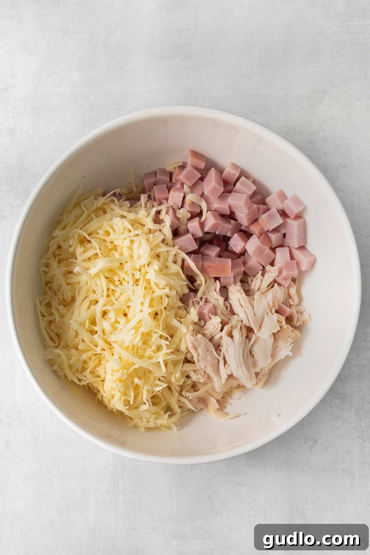 A large bowl containing mixed ingredients for chicken cordon bleu casserole, including shredded chicken, ham, and Swiss cheese, ready to be transferred to a baking dish.