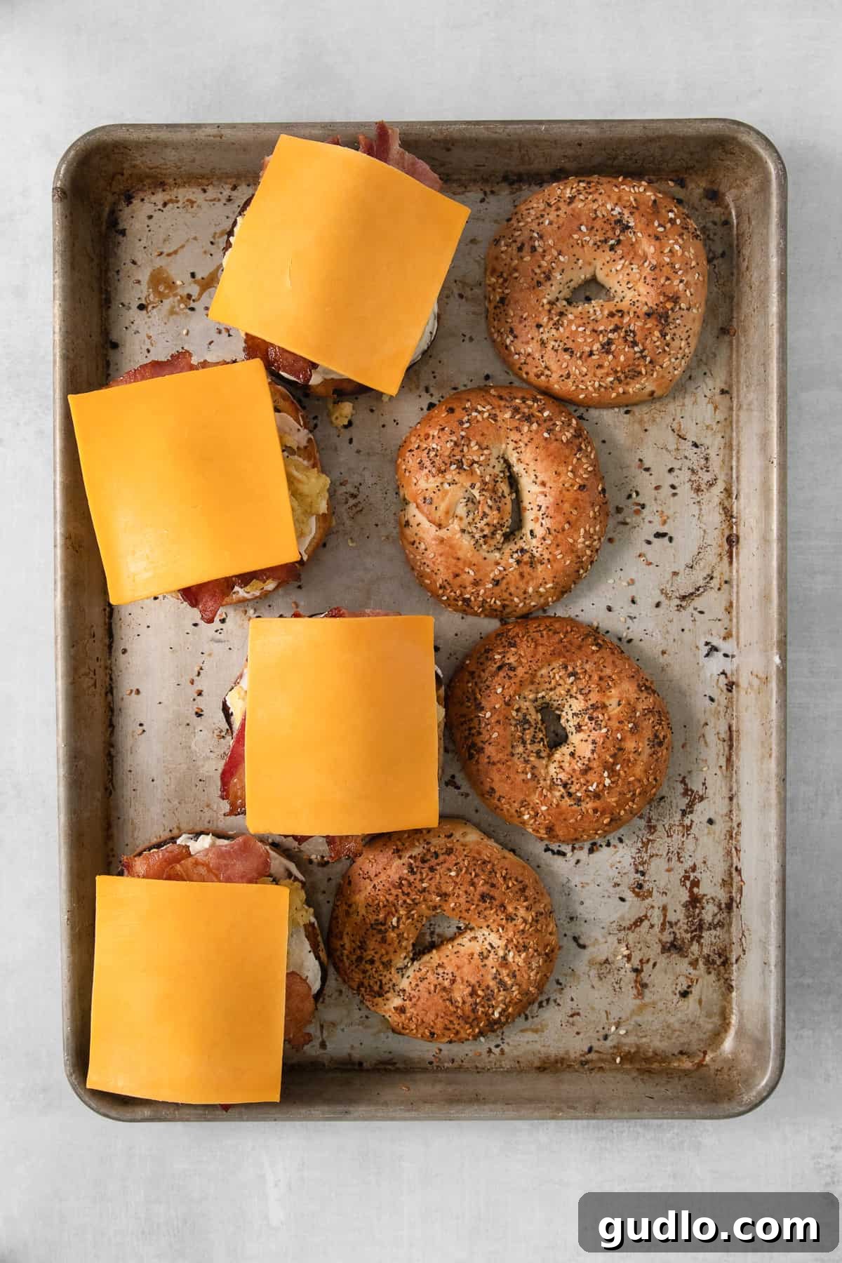 Hearty Morning Bagel Stack 3 Various bagel breakfast sandwich ingredients, including bagels, bacon, and cheese, neatly arranged on a baking sheet.