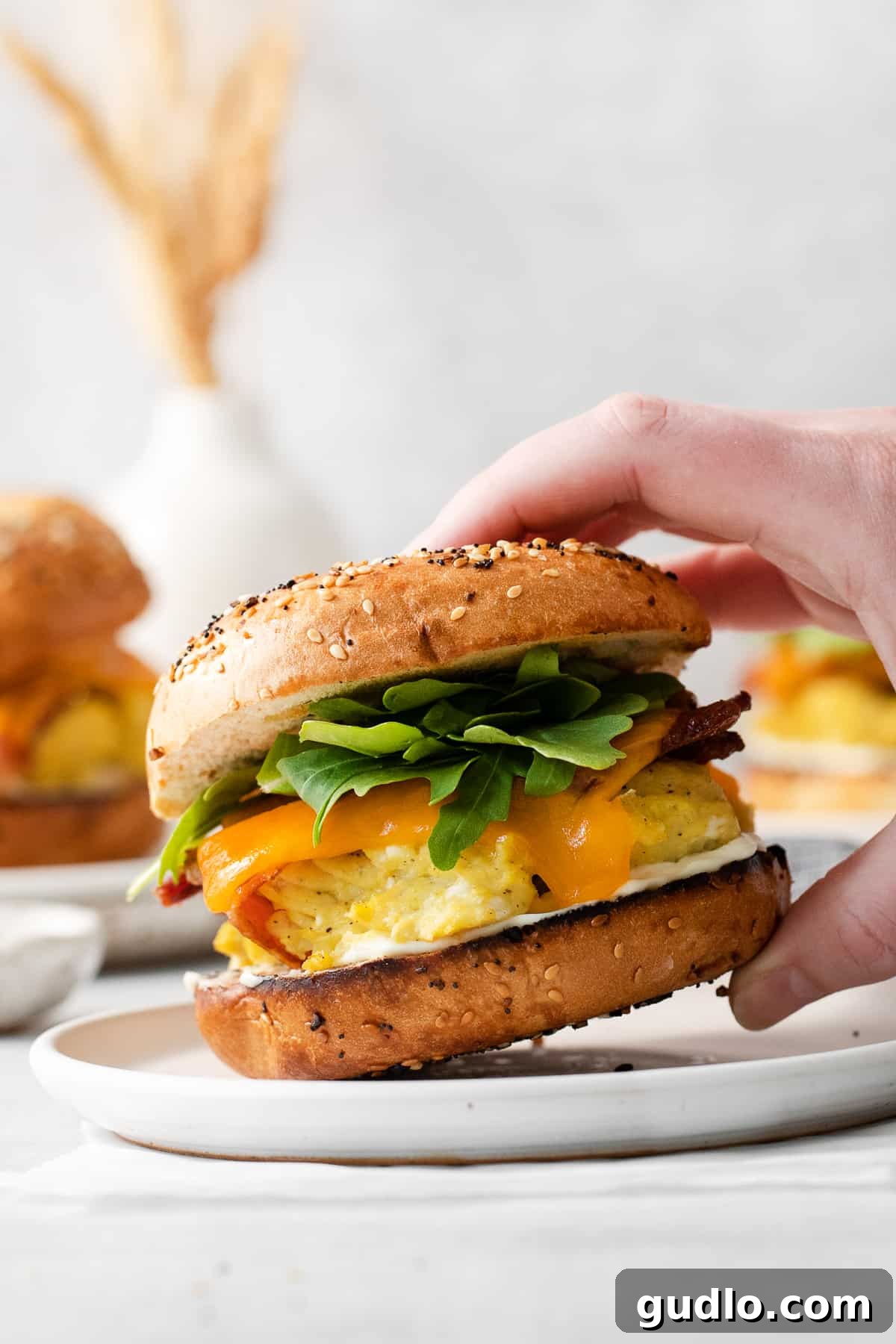 Hearty Morning Bagel Stack 7 A vibrant bagel breakfast sandwich garnished with fresh arugula on a white plate, highlighting a fresh, healthy addition.