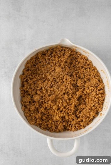 a white dish with a brown crumble in it, showing the crust mixture.