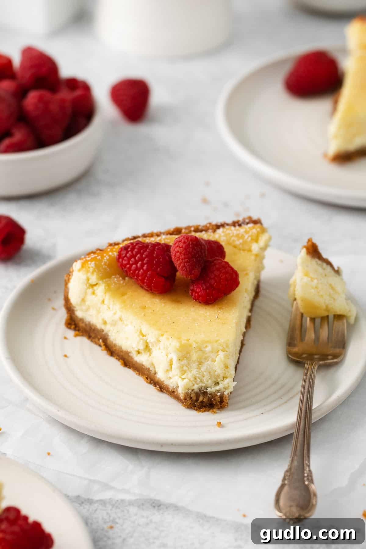 A perfectly sliced piece of ricotta cheesecake on a plate, garnished with raspberries.