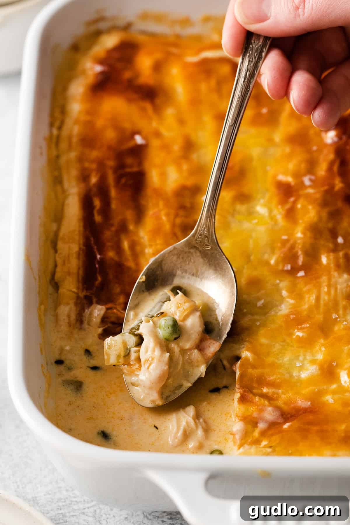 Hearty Chicken Pot Pie Casserole with Golden Puff Pastry A spoonful of creamy chicken pot pie casserole with a golden puff pastry crust.