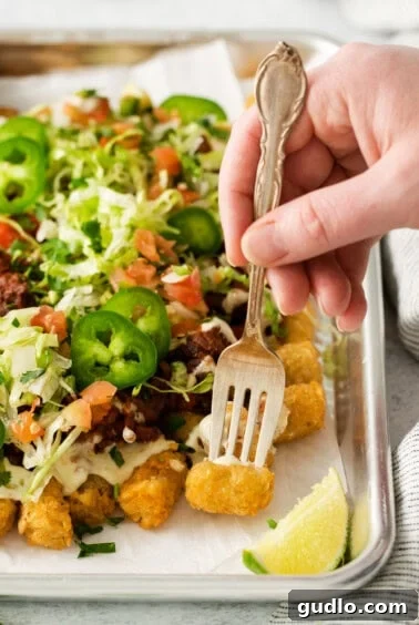No-Fuss Totchos 6 A hand holding a fork, poised over a freshly topped tray of totchos, ready to enjoy.