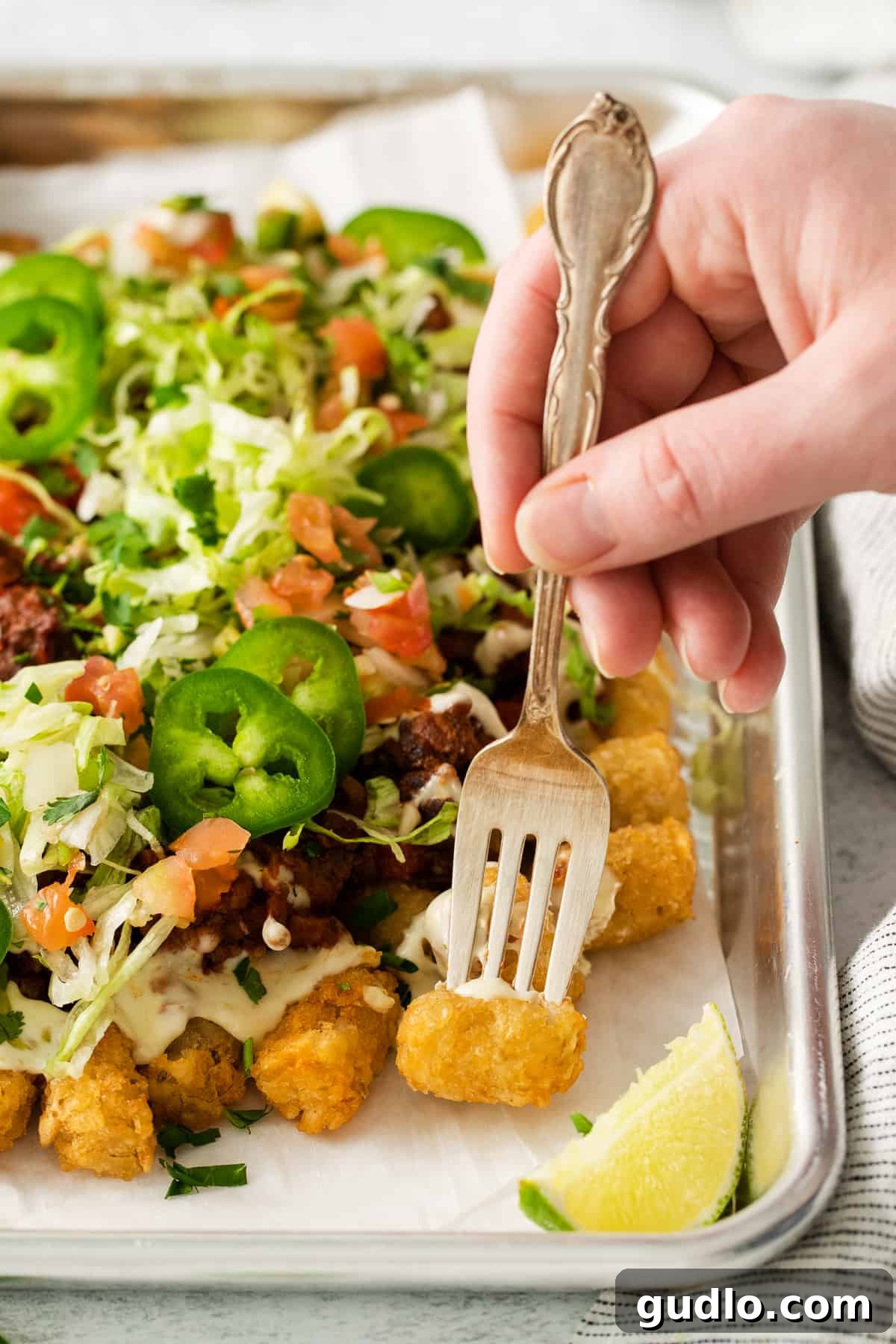 Loaded Tater Tot Nachos A single totcho perfectly balanced on a fork, showcasing its delicious layers.