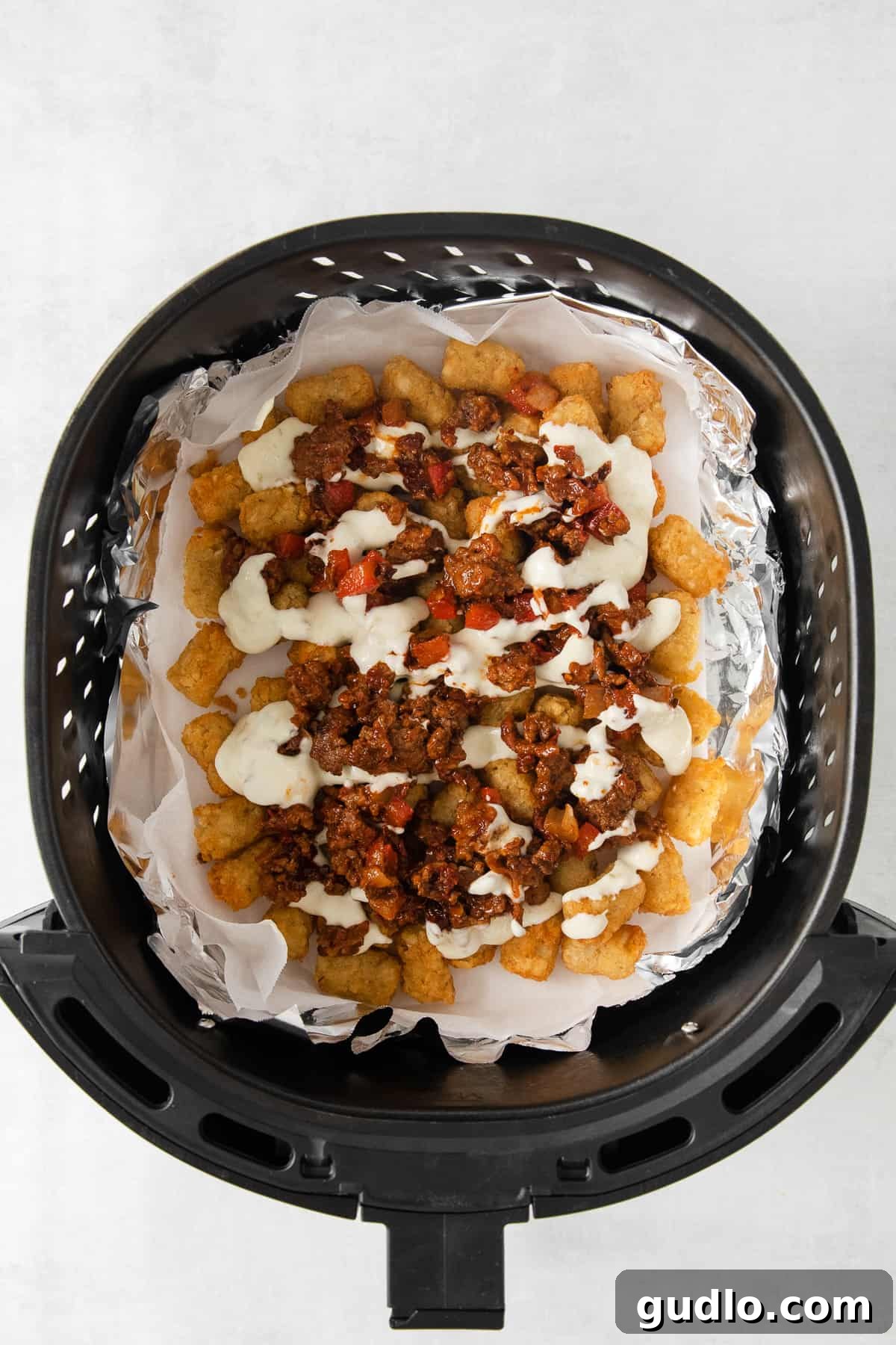 Assembled Totchos in Air Fryer Delicious totchos loaded with beef and melted cheese, sizzling in an air fryer basket.