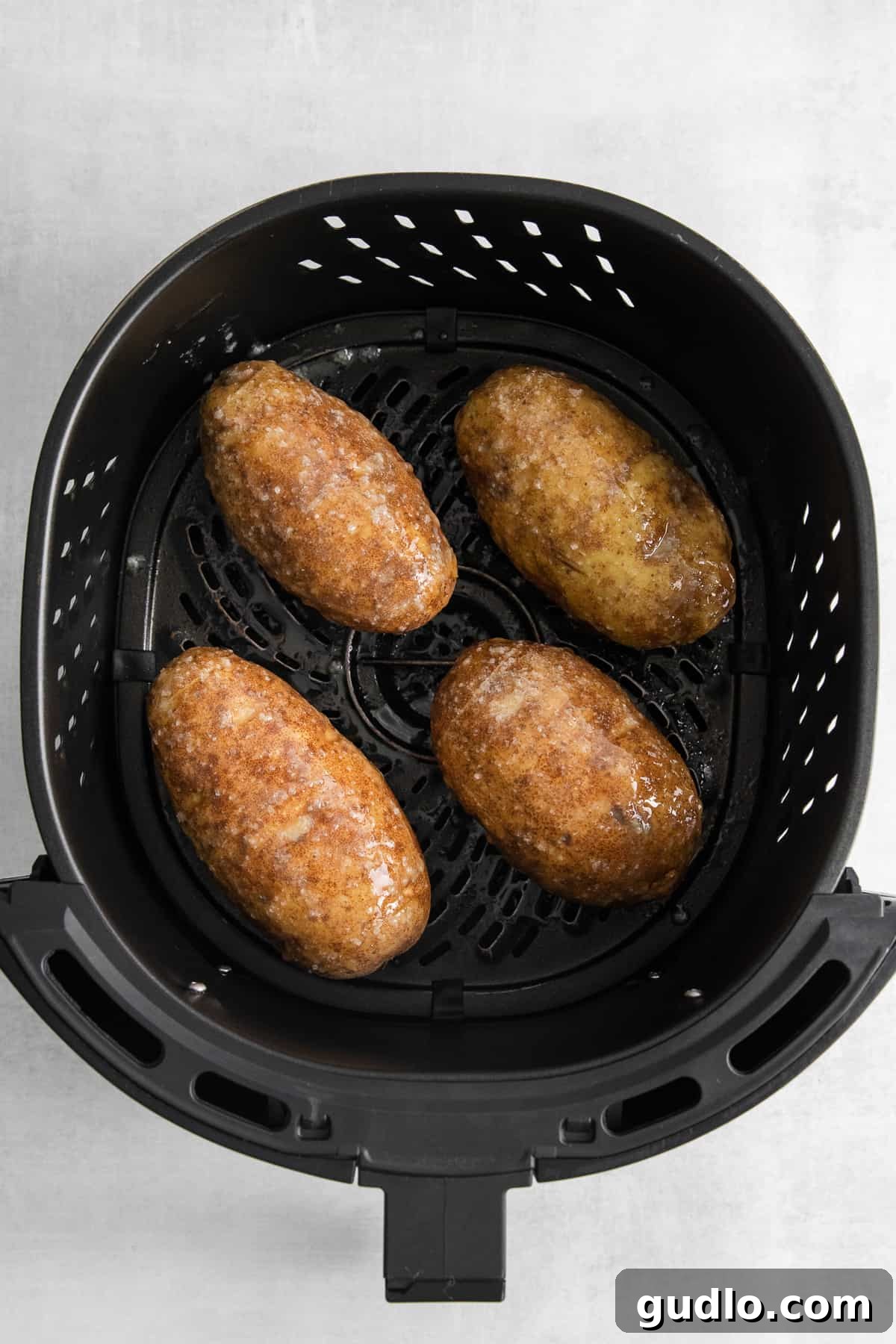 Oiled Hasselback Potatoes in Air Fryer Basket Raw hasselback potatoes generously oiled and ready to be air fried.