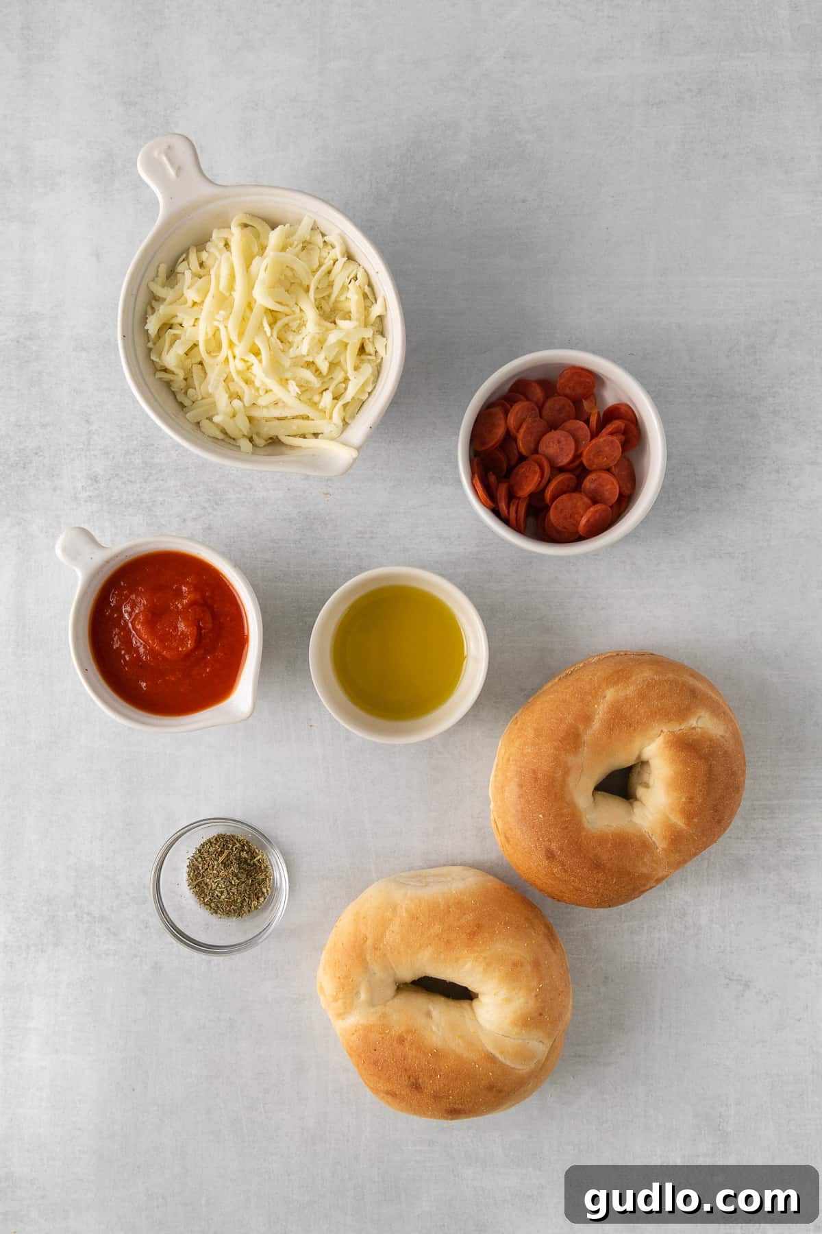 Fresh ingredients ready for quick and easy air fryer pizza bagels. A vibrant flat lay of fresh ingredients for air fryer pizza bagels, including bagels, a bowl of pizza sauce, shredded mozzarella cheese, mini pepperoni, and Italian seasoning.