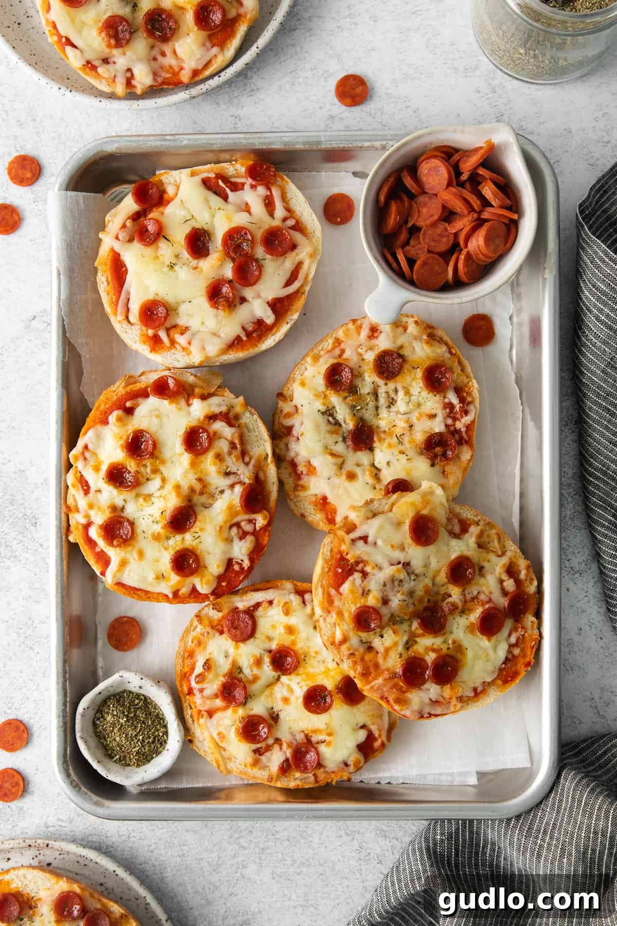 Oven-baked pizza bagels, golden and cheesy on a baking tray. Freshly baked pizza bagels, glistening with melted cheese and pepperoni, resting on a parchment-lined baking sheet after being cooked in the oven.